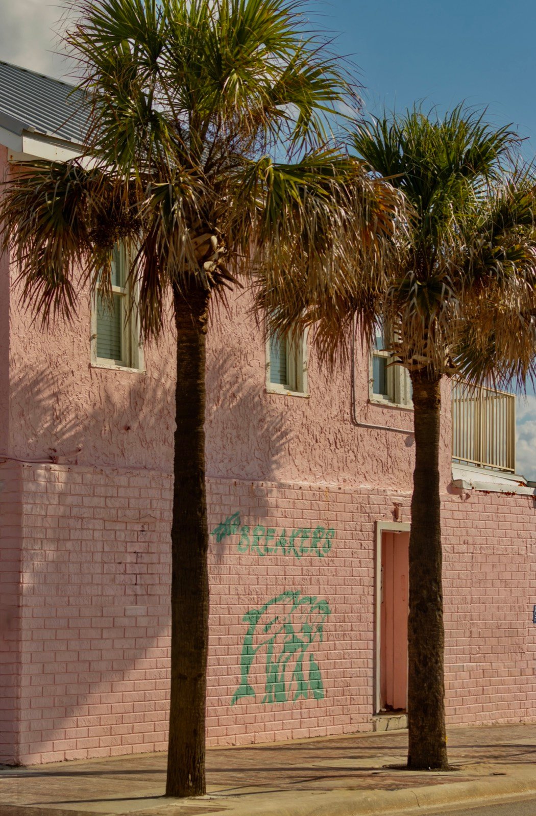 The side of the pink Breakers building with palm trees against the Florida sky